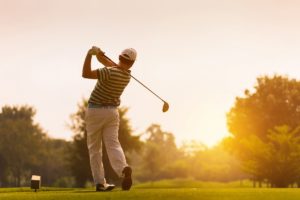 Man in mid golf swing in front of sunset